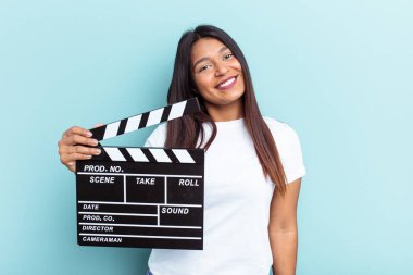 Genç Venezuelalı bir kadın mavi arka planda izole edilmiş bir alçıpan tutuyor. Mutlu, gülümseyen ve neşeli..