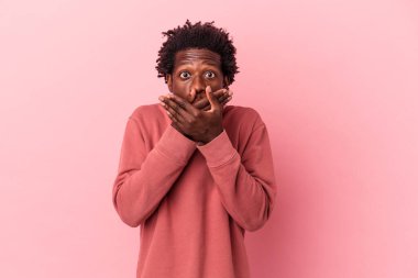 Pembe arka planda izole edilmiş genç Afrikalı Amerikalı adam elleriyle ağzını kapatırken şok oldu..