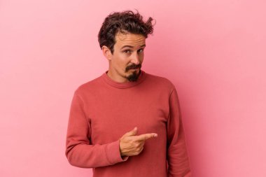 Pembe arka planda izole edilmiş genç beyaz adam gülümsüyor ve boş alanda bir şeyler gösteriyor..