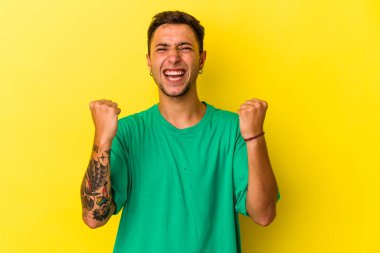 Sarı arka planda izole edilmiş dövmeleri olan, tasasız ve heyecanlı genç beyaz bir adam. Zafer konsepti.