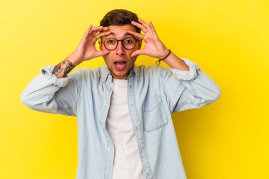 Sarı arka planda izole edilmiş dövmeleri olan beyaz genç bir adam başarılı bir fırsat yakalamak için gözlerini açık tutuyor..