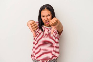 Beyaz arka planda izole edilmiş genç Latin bir kadın baş parmağını aşağı gösteriyor ve hoşlanmadığını ifade ediyor..
