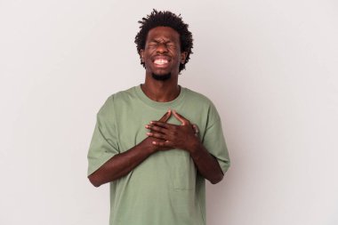 Genç Afrikalı Amerikalı adam beyaz arka planda soyutlanmış gülüyor, ellerini yüreğine koyuyor, mutluluk kavramını koruyor..