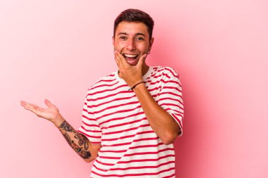 Sarı arka planda dövmeleri olan beyaz bir genç avucunun içinde fotokopi alanı tutuyor, el üstünde tutuyor. Şaşırmış ve mutlu..