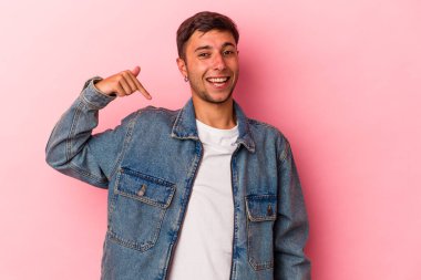 Sarı arka planda izole edilmiş beyaz dövmeli genç bir adam gömlek fotokopi alanını işaret ediyor, gururlu ve kendinden emin.