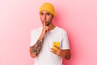 Pembe arka planda cep telefonu tutan genç beyaz adam bir sır saklıyor ya da sessizlik istiyor..