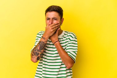 Sarı arka planda dövmeleri olan beyaz genç bir adam virüs ya da enfeksiyon yüzünden boğazında ağrı hissediyor..