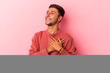 Sarı arka planda izole edilmiş dövmeleri olan genç beyaz bir adam gülüyor, ellerini yüreğine koyuyor, mutluluk kavramını koruyor..