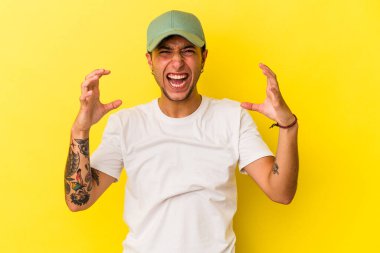 Sarı arka planda izole edilmiş dövmeleri olan genç beyaz bir adam öfkeyle bağırıyor..