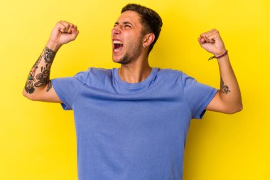 Sarı arka planda izole edilmiş beyaz dövmeli genç bir adam zaferden sonra yumruğunu kaldırıyor, kazanan konsept.