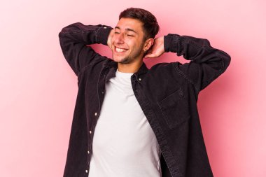 Sarı arka planda izole edilmiş, elleri başının arkasında kendinden emin dövmeleri olan genç, beyaz bir adam..