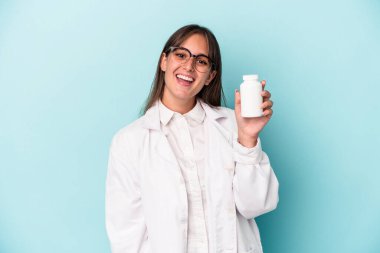 Mavi arka planda hapları tutan genç eczacı kadın mutlu, güler yüzlü ve neşeli..