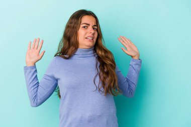 Genç beyaz kadın, mavi arka planda izole edilmiş. Yakın bir tehlike nedeniyle şoka uğruyor.