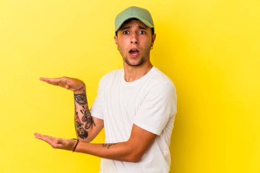Sarı arka planda izole edilmiş beyaz dövmeli genç bir adam elleri arasında bir kopya alanı tutarken şok ve hayrete düştü..