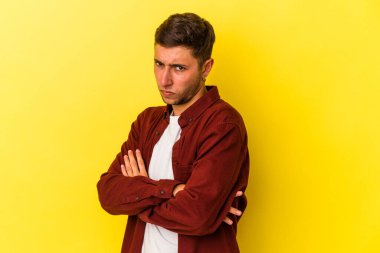 Sarı arka planda izole edilmiş dövmeleri olan genç beyaz bir adam tekrarlanan bir görevden yoruldu..