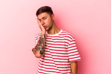 Sarı arka planda dövmeleri olan, sıkılmış, yorgun ve dinlenmeye ihtiyacı olan beyaz bir genç adam..