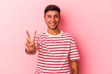 Sarı arka planda dövmeleri olan genç beyaz bir adam iki numarayı parmaklarıyla gösteriyor..