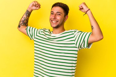 Sarı arka planda izole edilmiş dövmeleri olan, tasasız ve heyecanlı genç beyaz bir adam. Zafer konsepti.
