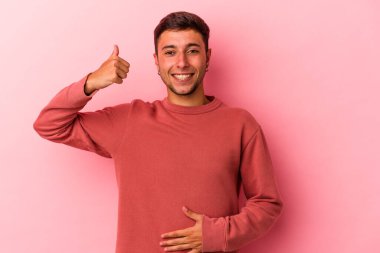 Sarı arka planda izole edilmiş beyaz dövmeli genç bir adam karnına dokunuyor, nazikçe gülümsüyor, yemek yiyor ve tatmin oluyor..