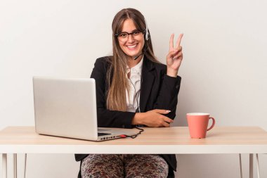 Beyaz arka planda seyahat eden beyaz tenli genç bir kadın iki numarayı parmaklarıyla gösteriyor..