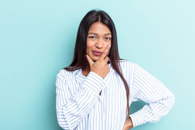 Genç Venezuelalı bir kadın, mavi arka planda izole edilmiş, bir strateji planlıyor, bir işin nasıl olacağını düşünüyor..