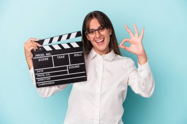 Elinde klaket tutan beyaz bir kadın mavi arka planda izole edilmiş neşeli ve kendinden emin bir şekilde iyi niyet gösteriyor..