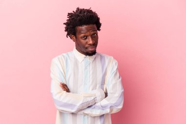 Genç Afro-Amerikalı, pembe arka planda izole edilmiş, mutsuz bir şekilde kameraya bakıp alaycı bir ifade takınıyor..