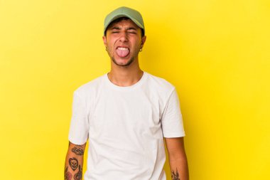 Sarı arka planda izole edilmiş beyaz dövmeli genç bir adam. Komik ve dost canlısı bir dil uzatıyor..