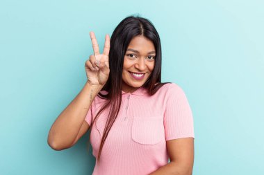 Genç Venezuelalı kadın mavi arka planda iki numarayı parmaklarıyla gösteriyor..