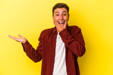 Sarı arka planda dövmeleri olan beyaz bir genç avucunun içinde fotokopi alanı tutuyor, el üstünde tutuyor. Şaşırmış ve mutlu..