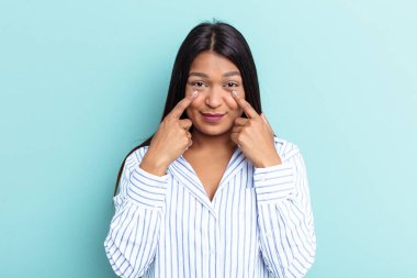 Genç Venezuelalı bir kadın mavi arka planda izole edilmiş, ağlıyor, bir şeyden mutsuz, acı ve karmaşa konsepti..