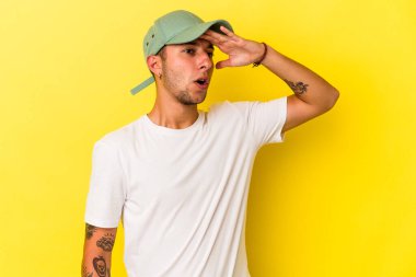 Sarı arka planda izole edilmiş dövmeleri olan genç, beyaz bir adam. Uzağa bakıyor. Alnını tutuyor..