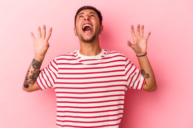 Sarı arka planda izole edilmiş dövmeleri olan genç beyaz adam gökyüzüne haykırıyor, yukarı bakıyor, hayal kırıklığına uğruyor..