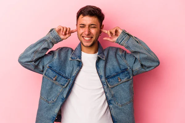 Sarı arka planda dövmeleri olan, kulaklarını parmaklarıyla kapatan, stresli ve çaresiz genç beyaz bir adam..