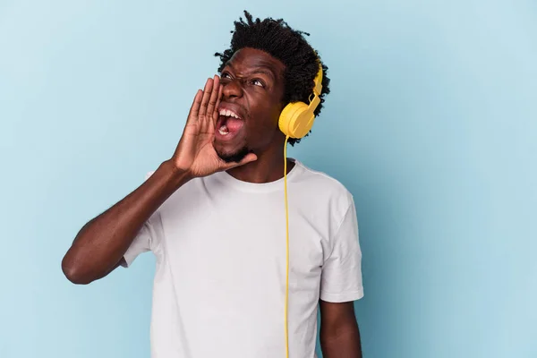 若いアフリカ系アメリカ人の男は青い背景の叫びに隔離された音楽に耳を傾け 手のひらを開いて口の近くに — ストック写真