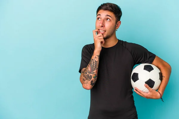 Młody Człowiek Gra Piłkę Nożną Trzymając Piłkę Niebieskim Tle Zrelaksowany — Zdjęcie stockowe