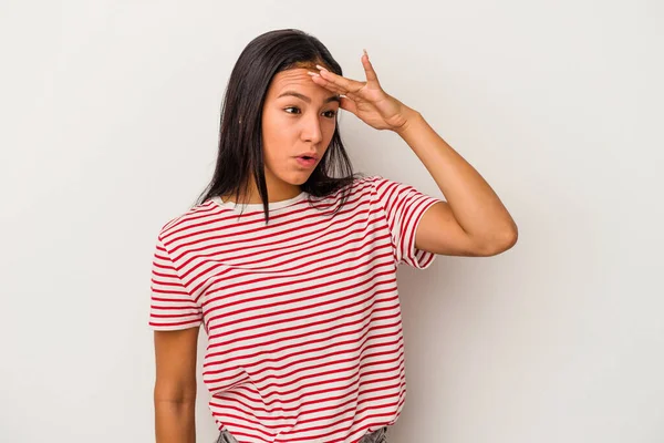 Beyaz arka planda izole edilmiş genç Latin kadın uzaklara bakıyor ve elini alnına koyuyor..