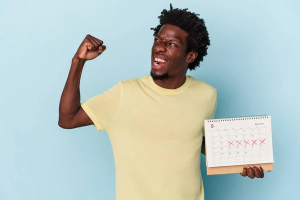 Mladý Africký Američan Drží Kalendář Izolované Modrém Pozadí Zvedání Pěst — Stock fotografie