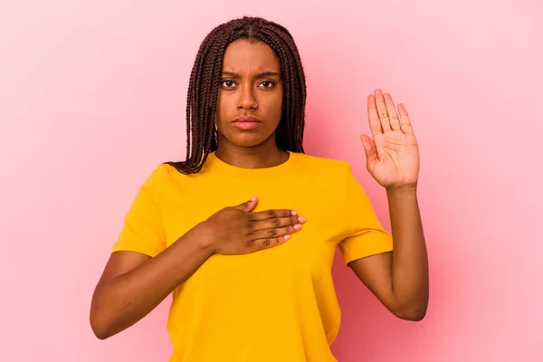 年轻的非洲裔美国女人 背景是粉色的 发过誓 双手放在胸前 — 图库照片