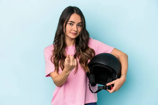 Young caucasian woman holding a motor bike helmet isolated on blue background pointing with finger at you as if inviting come closer.