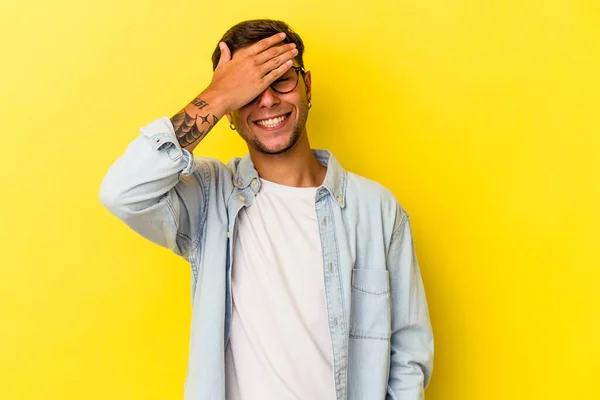 Mladý Běloch Tetováním Izolovaným Žlutém Pozadí Zakrývá Oči Rukama Usmívá — Stock fotografie