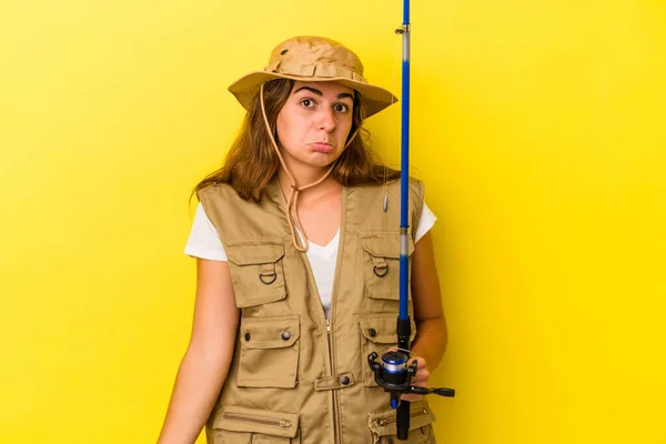 Young Caucasian Fisherwoman Holding Rod Isolated Yellow Background Shrugs Shoulders — Stock Photo, Image