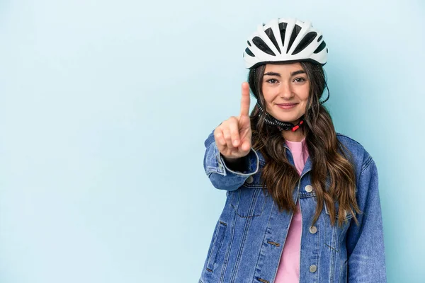 Young caucasian woman rinding a bike isolated on blue background showing number one with finger.