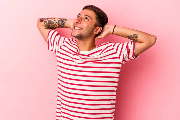 Sarı arka planda izole edilmiş, elleri başının arkasında kendinden emin dövmeleri olan genç, beyaz bir adam..