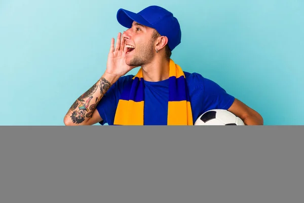 Mladý Fotbalový Fanoušek Muž Drží Míč Izolovaný Modrém Pozadí Křičí — Stock fotografie