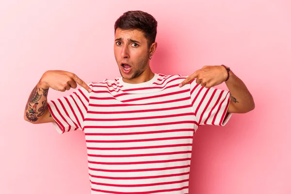 Sarı arka planda izole edilmiş dövmeleri olan beyaz bir genç. Parmakları aşağıda, olumlu hisler içinde..