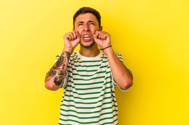 Sarı arka planda izole edilmiş, ağlayan ve sızlanan, dövmeleri olan beyaz bir genç..