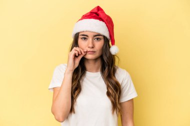 Sarı arka planda izole edilmiş, dudakları dudaklarında bir sırrı saklayan genç beyaz kadın Noel 'i kutluyor..