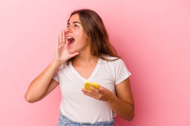 Pembe arka planda izole edilmiş cep telefonu kullanan beyaz bir kadın bağırıyor ve avuç içini açık tutuyor..