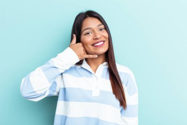 Genç Venezuelalı bir kadın mavi arka planda izole edilmiş, parmakları olan bir cep telefonu hareketi gösteriyor..